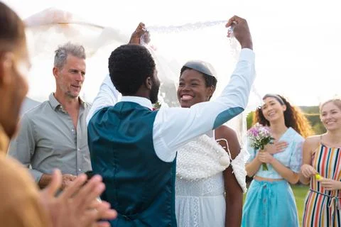 Happy african american couple holding veil and smiling during wedding Stock Photos