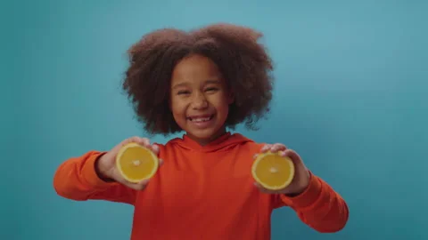 Happy African American girl holding two orange fruit halves in hands and dancing Stock Footage