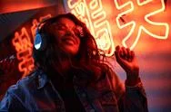 Happy African American Lady Wearing Headphones Listening Music In Neon Light. Stock Photos