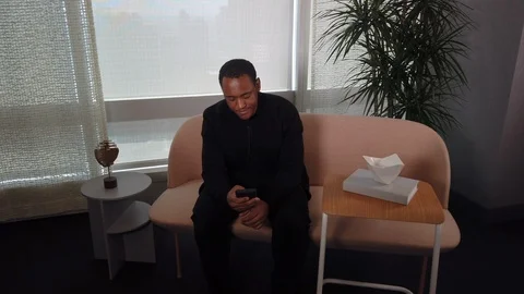 Happy African American Man using app on cell phone while sitting on sofa. 스톡 동영상 108601247