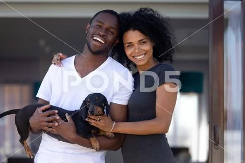 Happy african millennial couple embrace outdoors holding pet, portrait Stock Photos