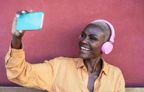 Happy African woman taking selfie with mobile smartphone while listening music Stock Photos