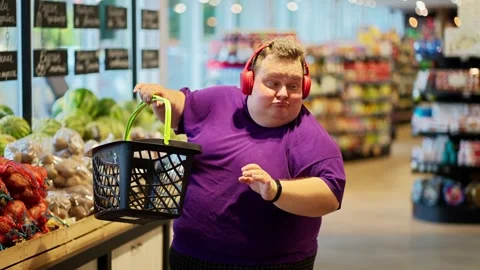 A happy and cheerful overweight man in a purple T-shirt and red headphones walks Vídeos de archivo 252183322
