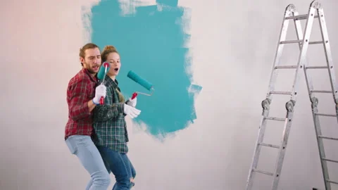 Happy and funny couple while painting the walls using the wall brush roller to Video stock 171220051