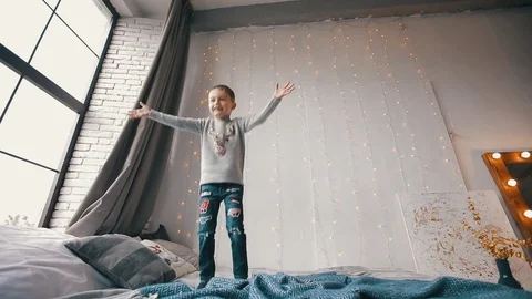 Happy and smiling boy jumping on a bed and catch a teddy bear Stock Footage 122585517