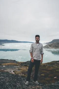 Happy and smiling young man standing in front of Eqip Sermia glacier called Eqi Stock Photos