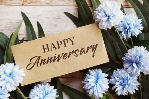 Happy Anniversary text message with flower decoration on wooden background Stock Photos