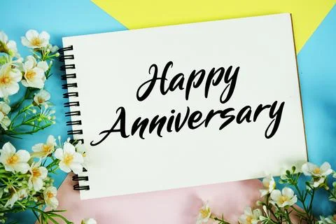 Happy Anniversary text written on notepad with flowers decorations flat lay.. Stock Photos