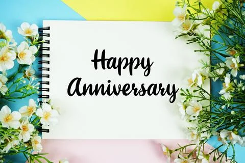 Happy Anniversary text written on notepad with flowers decorations flat lay.. Stock Photos
