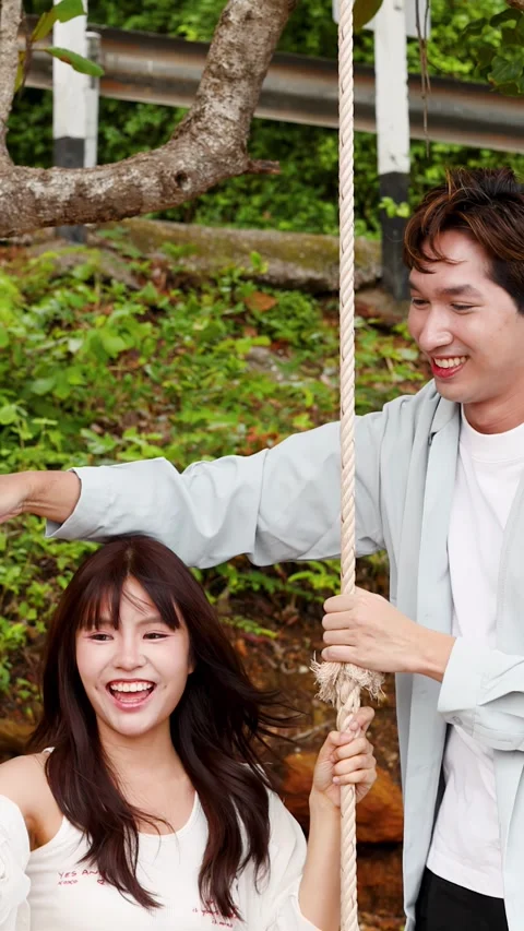 Happy Asian Couple Having Fun on Tree Swing Outdoors Stock Footage 346452887
