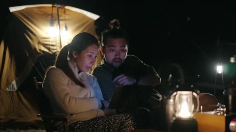 Happy Asian couple using a smartphone while camping at night Stock Footage 168484601