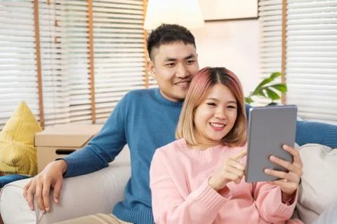Happy asian couple using tablet to design decorate new house interior at sofa Stock Photos