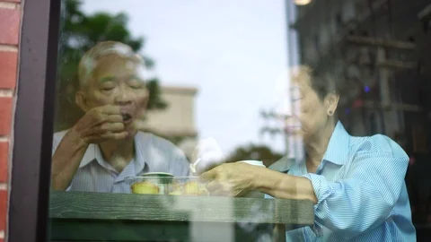 Happy Asian elderly couple drinking morning coffee through cafe glass front Stock Footage 94484385