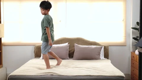 Happy asian elementary school boy jumping and dancing on bed, kid jumped an.. Stock Footage 249443874