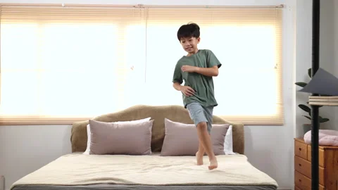 Happy asian elementary school boy jumping and dancing on bed, kid jumped an.. Stock Footage 249505744