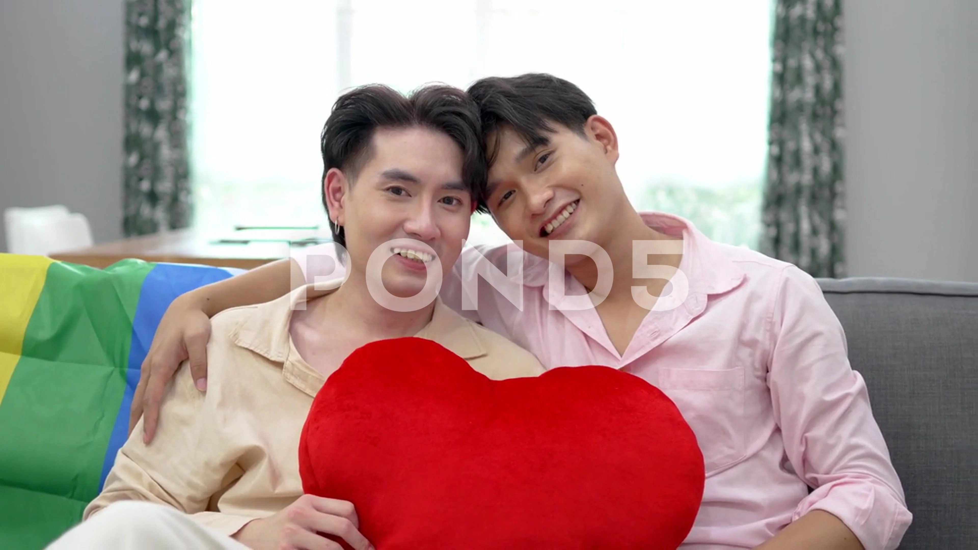 Happy Asian gay couple embracing and showing their love with red heart  pillows