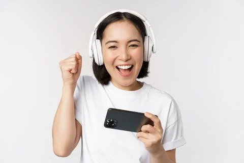 Happy asian girl gamer, playing on mobile phone, watching on smartphone, wearing Stock Photos