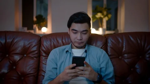 Happy Asian guy thinking about what to write up in chat on mobile phone. Stock Footage 105752763