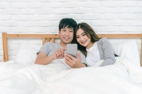 Happy Asian Lover using the technology smart phone on the bed in bedroom at h Stock Photos
