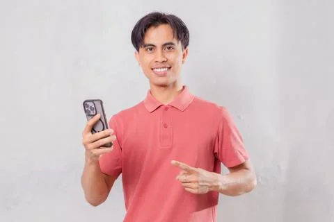 Happy Asian man pointing at smartphone isolated on plain background Stock Photos