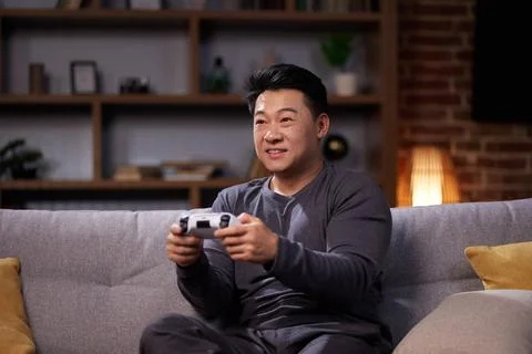 Happy Asian man using a wireless joystick and playing video games at home Stock Photos