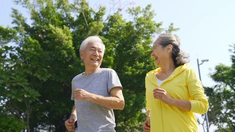 Happy asian old couple jogging outdoors in a park Stock Footage