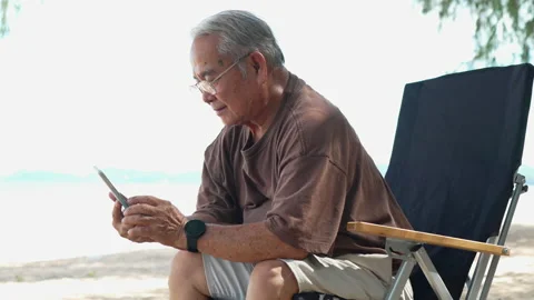 Happy asian senior elderly using smartphone technology outside on the beach Stock Footage 199264933