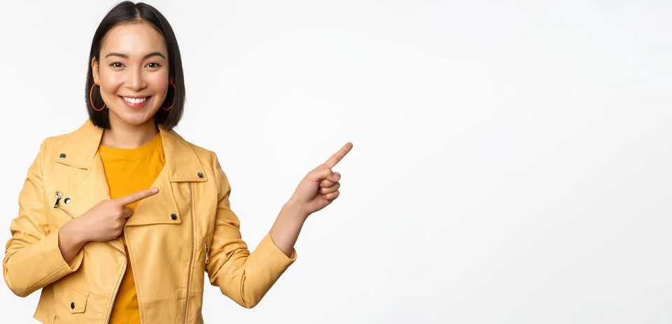 Happy asian woman smiling, pointing fingers right, inviting to check out sale Stock Photos