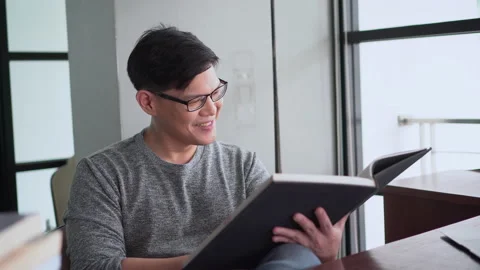 Happy asian young man reading a book and laughing  in Living room at home Stock Footage 158790890