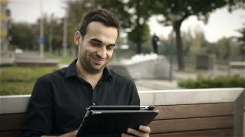 Happy attractive man using tablet PC outside on a park bench Vidéo 42164056
