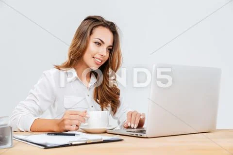 Happy attractive young businesswoman drinking coffee and using laptop Stock Photos