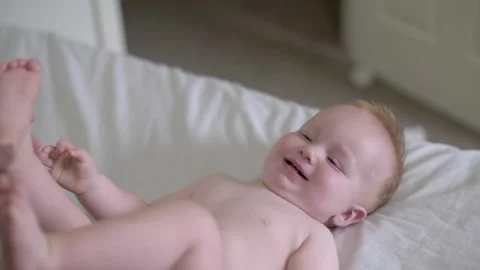 A happy baby laughing while lying on a bed, capturing a moment of joy and Видео 278017545