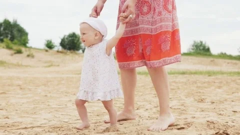 Happy baby is making the first steps with the mother on the sandy beach Video stock 83958401