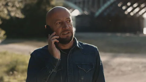 Happy bald and handsome man in his mid-forties is standing in teh park. He has a Stock Footage 144840391