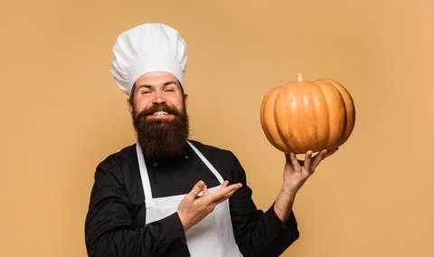 Happy bearded man in chef hat and uniform presenting big pumpkin for restaura Stock Photos