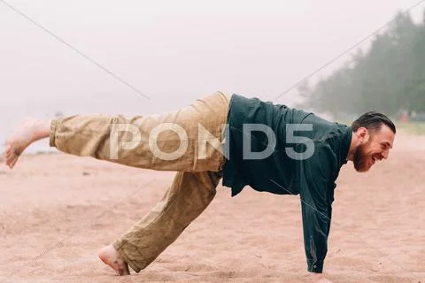 Happy bearded man does morning exercises at the beach Stock Photos