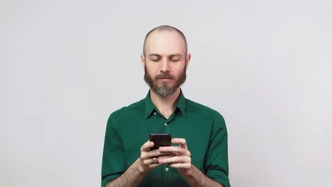 Happy bearded man looking surprised using mobile phone over white background. 動画素材 127425636