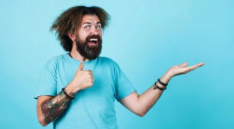 Happy bearded man presenting something on palm hand and showing thumb up. Adv Stock Photos
