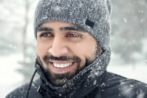 Happy bearded Middle eastern man wearing winter clothes under the snow Stock Photos