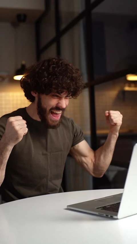 Happy bearded young man working at laptop at home and celebrating victory with Video stock 150052636