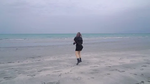 Happy beautiful blonde woman walks along the beach, cold rainy weather, autumn Stock Footage
