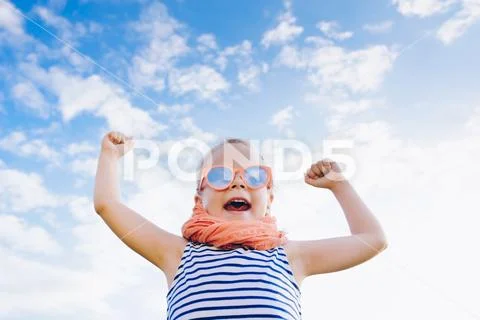 Happy beautiful child girl in sunglasses with raised arms against the sky Stock Photos