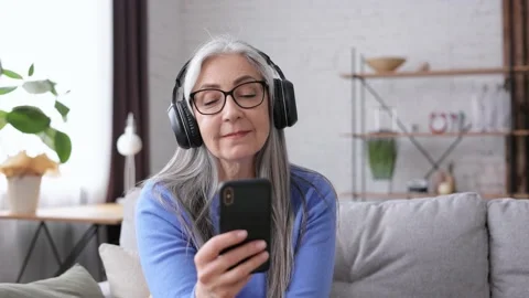 Happy beautiful elderly gray-haired woman in black headphones enjoy listening Video stock 164532955