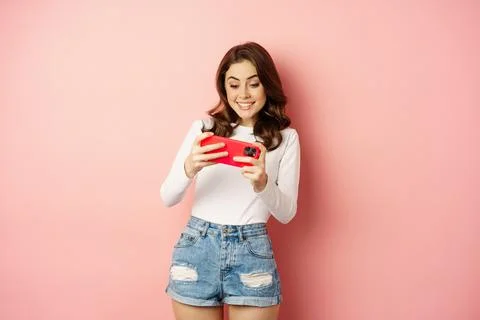 Happy beautiful girl playing mobile video game, holding smartphone horizontally Stock Photos