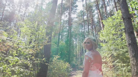 Happy beautiful smiling bride walking in sunny forest and looking around Stock Footage 59109029