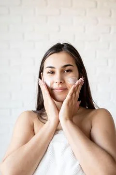 Happy beautiful woman wearing bath robes applying facial cream on her face Stock Photos
