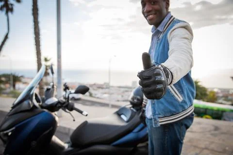 A happy biker shows thumbs up while standing by his scooter, road safety co.. Foto stock
