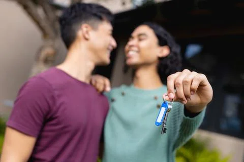 Happy biracial lgbt male couple moving house, embracing and holding house keys Stock Photos
