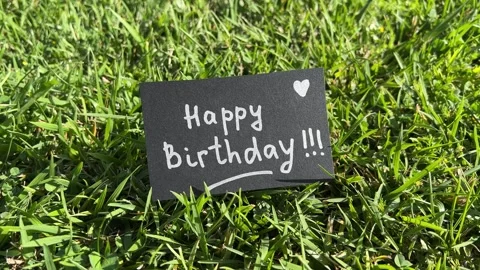 Happy birthday - black note with celebration text on the grass in the background Vidéo 339510395