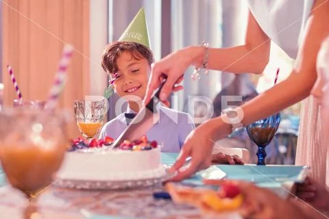 Happy birthday boy smiling while looking at the process of slicing cake Stock Photos